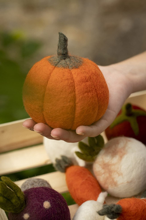 a hand is holding a pumpkin made of felt