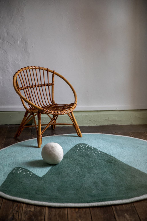 Round blue felt carpet with mountain print and small wicker chair for a natural decoration of the child's room Round blue felt carpet with mountain print and small wicker chair for a natural decoration of the child's room