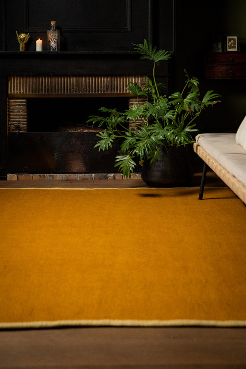 Tapis rectangle ocre en laine feutrée avec bordure jaune dans un salon