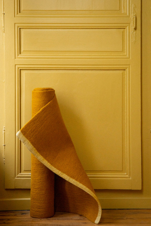 Tapis rectangle ocre en feutre de laine roulé devant une porte Tapis rectangle ocre en feutre de laine roulé devant une porte