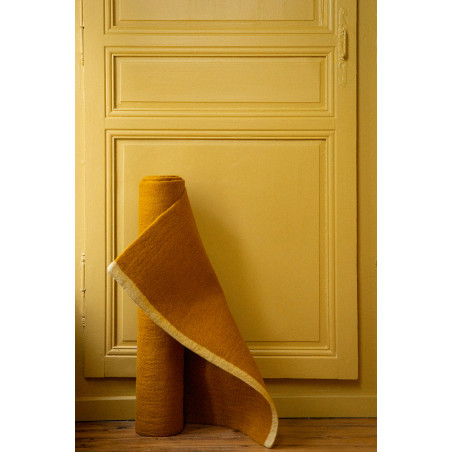 Tapis rectangle ocre en feutre de laine roulé devant une porte