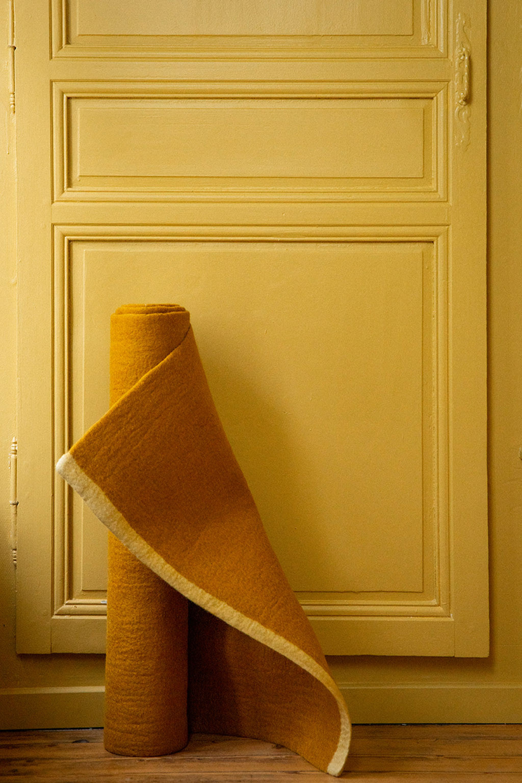 Tapis rectangle ocre en feutre de laine roulé devant une porte