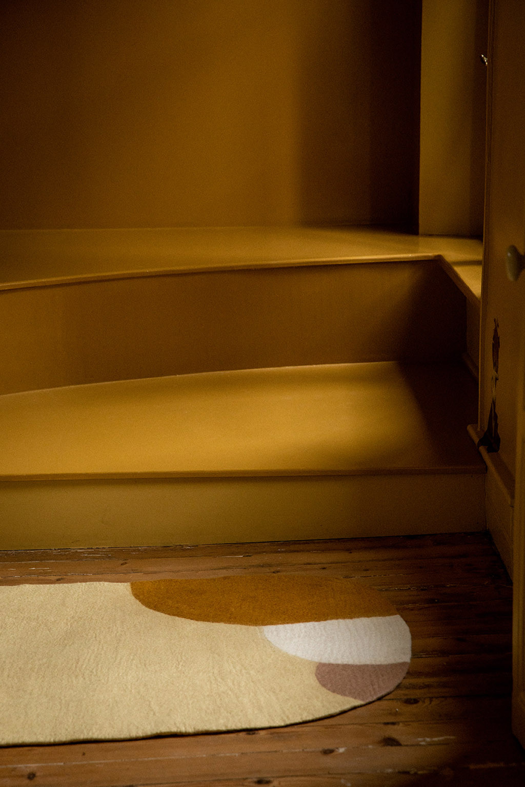 Tapis ovale en feutre jaune avec détails ocres, blancs et roses pour une décoration colorée