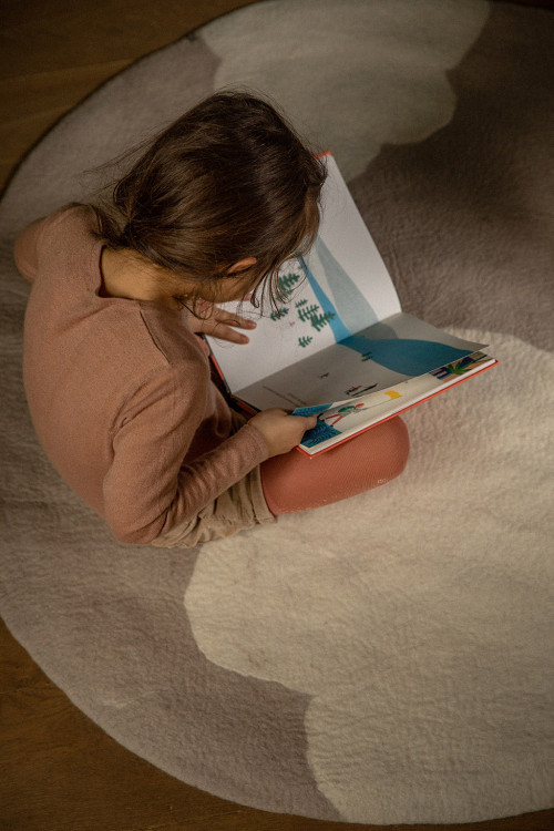 Petite fille lisant sur un tapis rond gris clair en laine feutrée avec imprimé nuage