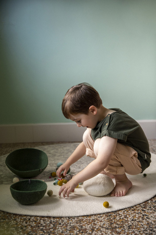 Little boy playing on a round white carpet with felted wool moon pattern