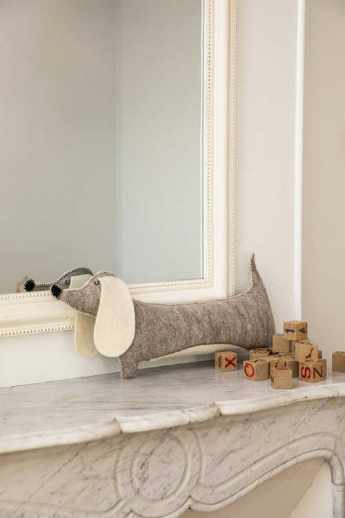 Coussin chien saucisse gris posé sur une cheminée avec quelques jouets