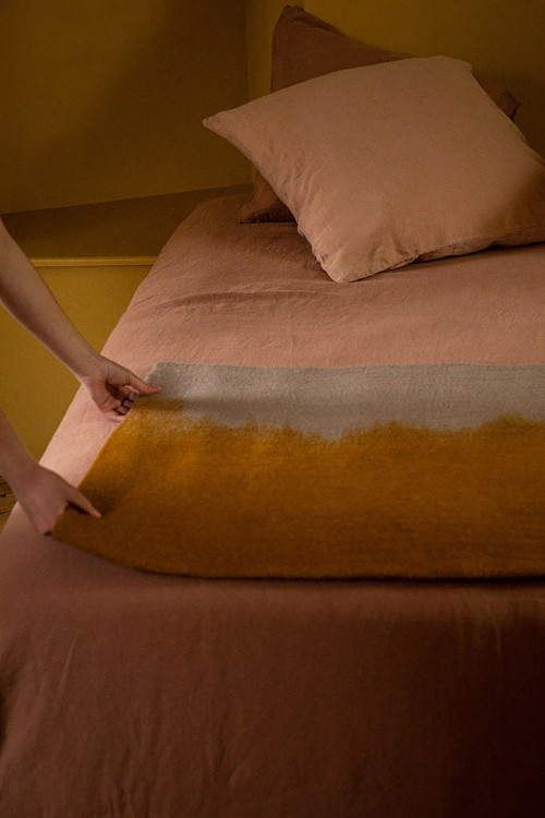 Tapis en feutre de laine jaune et gris posé sur un lit