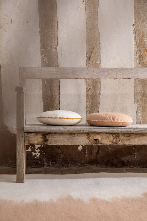 Rectangular felt carpet with pink and white felted wool cushions placed on a wooden bench