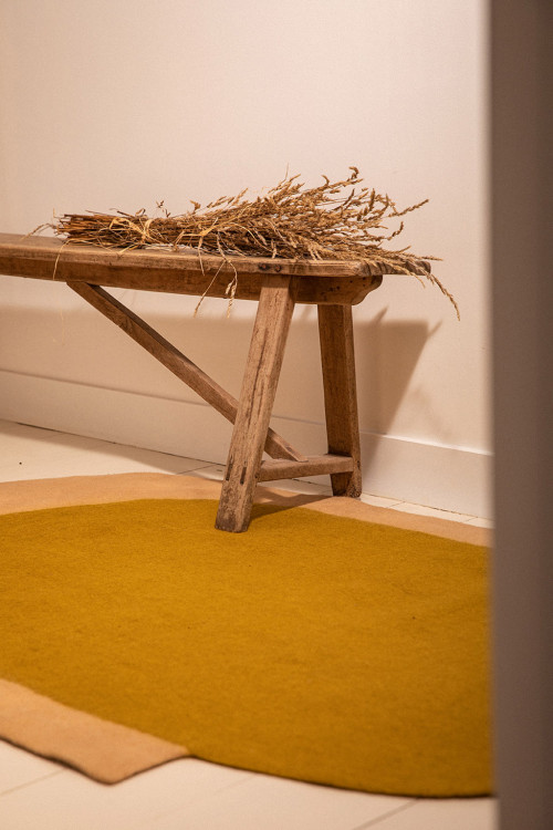 Tapis ovale en laine feutée rose et vert et banc en bois avec un bouquet de fleurs séchées