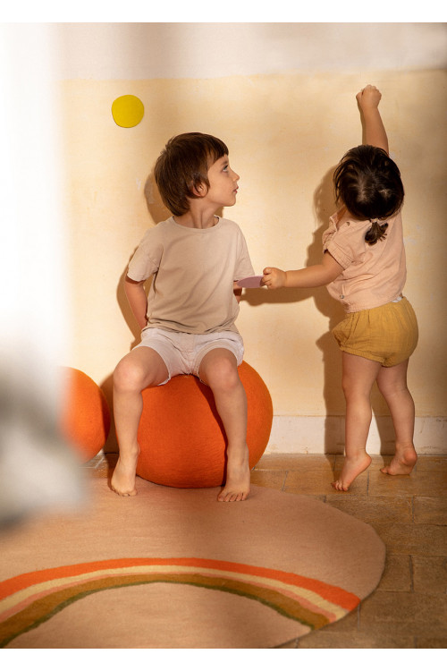 Round carpet with rainbow pattern and wool pouf for a playful bedroom decoration