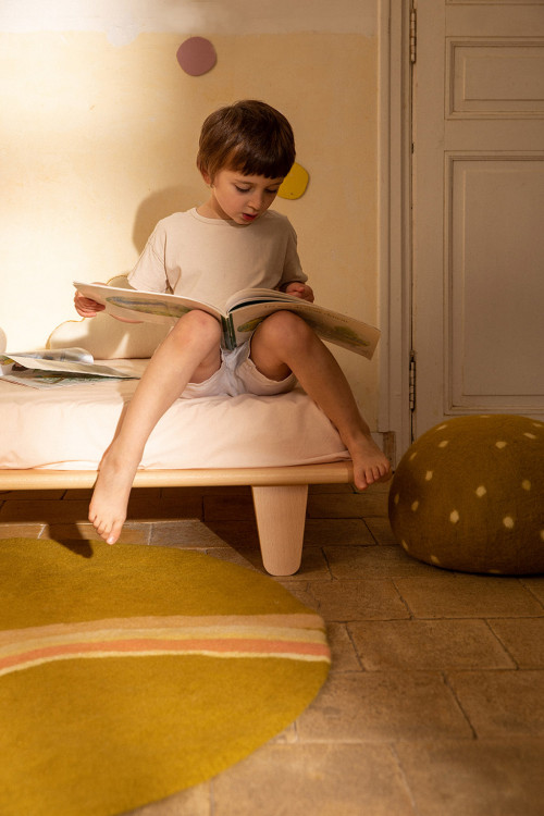 Round green felted wool rug with colorful rainbow pattern and little boy reading a book