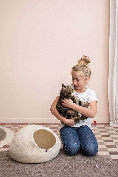 a girl strokes the cat next to her boiled wool cat basket
