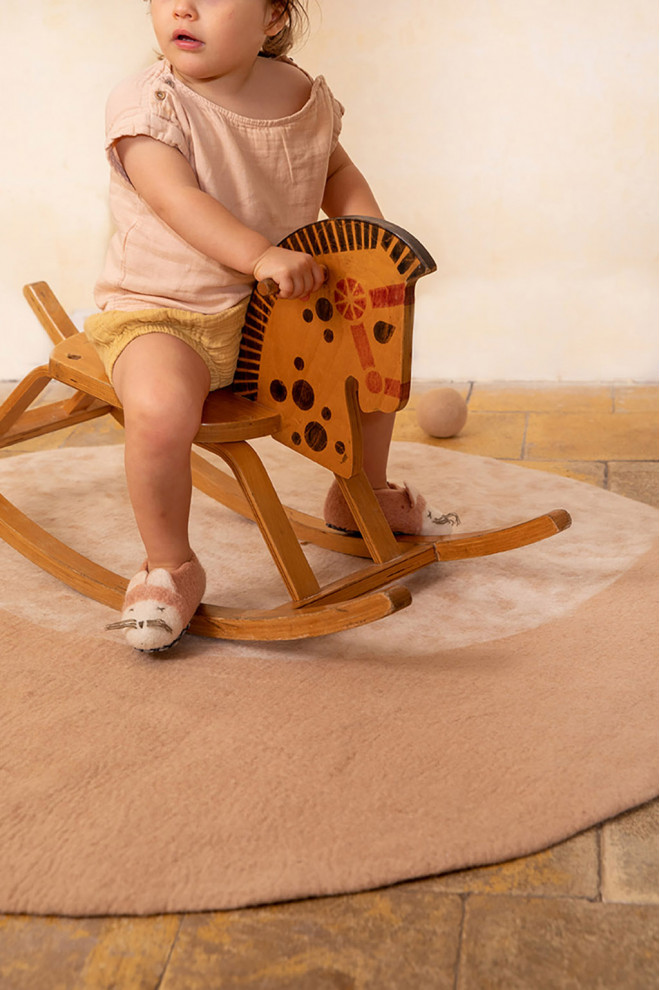 Petite fille avec un cheval bascule sur un tapis rond en feutre rose avec un imprimé lune