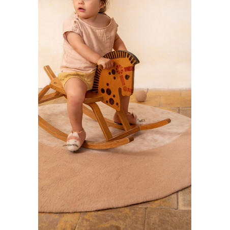 Little girl with a rocking horse on a round pink felt carpet with a moon print