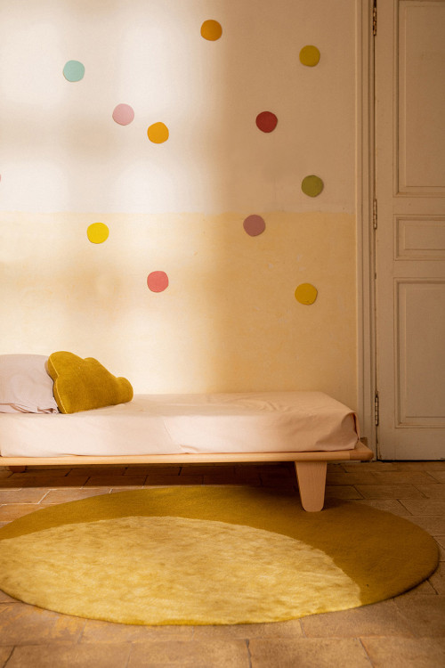 Round green felt carpet with moon motif at the foot of a child's bed