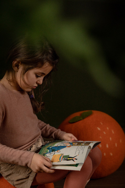 Petite fille lisant un livre assise sur un pouf clémentine