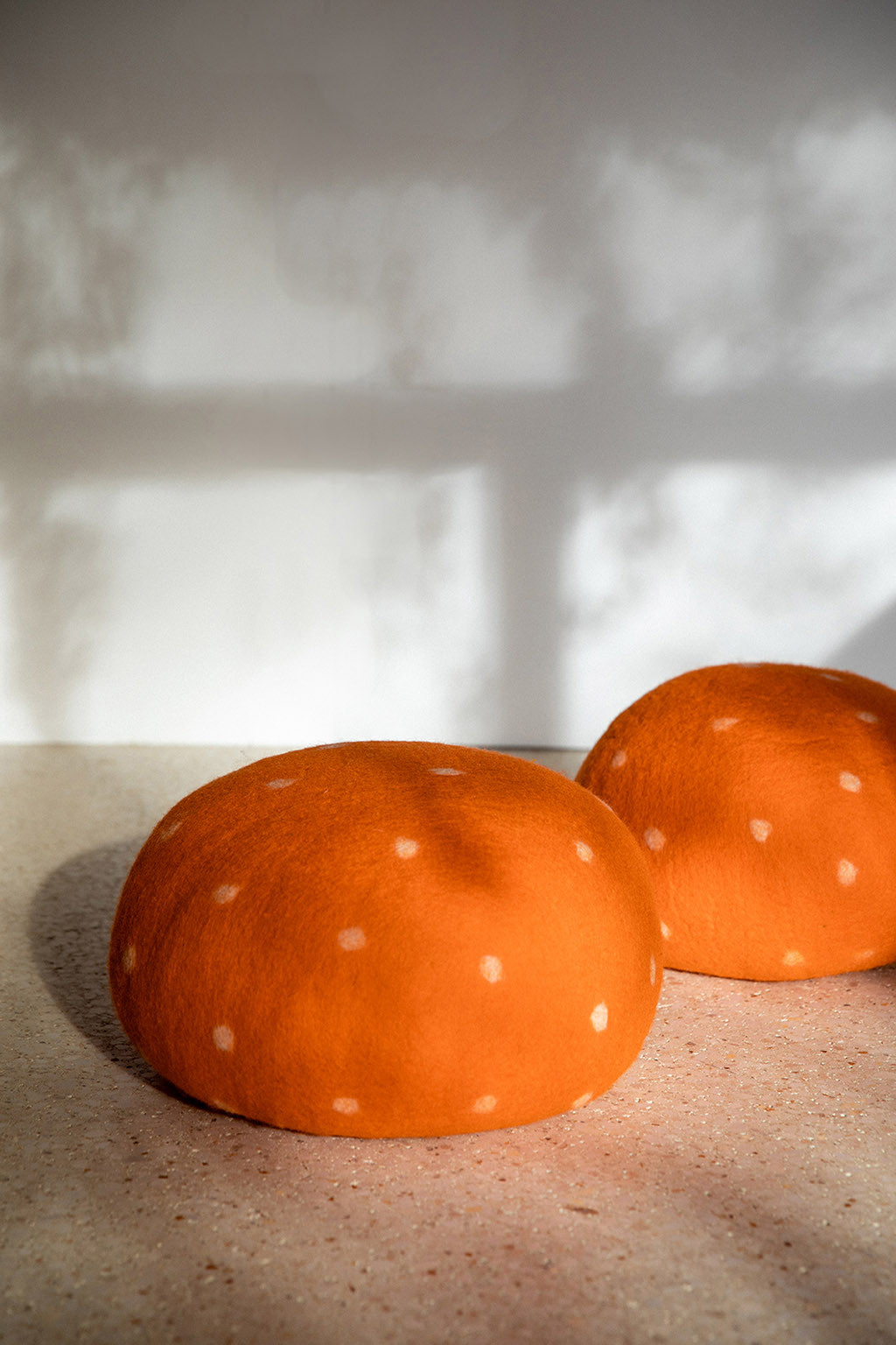 Two orange felted wool poufs reminiscent of mushrooms