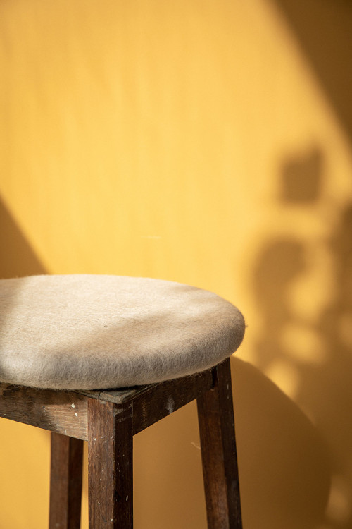 Round felted wool cushion on a wooden stool Round felted wool cushion on a wooden stool