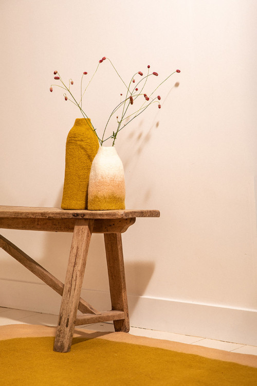 Duo de cache-vases colorés en laine bouillie posé sur un banc en bois Duo de cache-vases colorés en laine bouillie posé sur un banc en bois