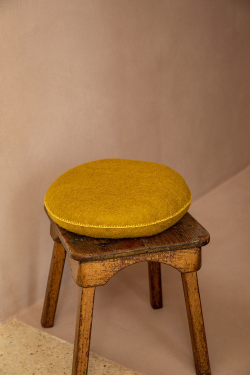 Un coussin pistache en laine bouillie sur un tabouret en bois Un coussin pistache en laine bouillie sur un tabouret en bois