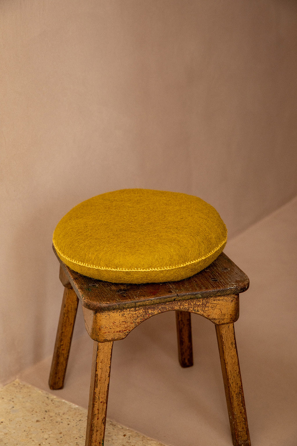 A pistachio cushion in boiled wool on a wooden stool
