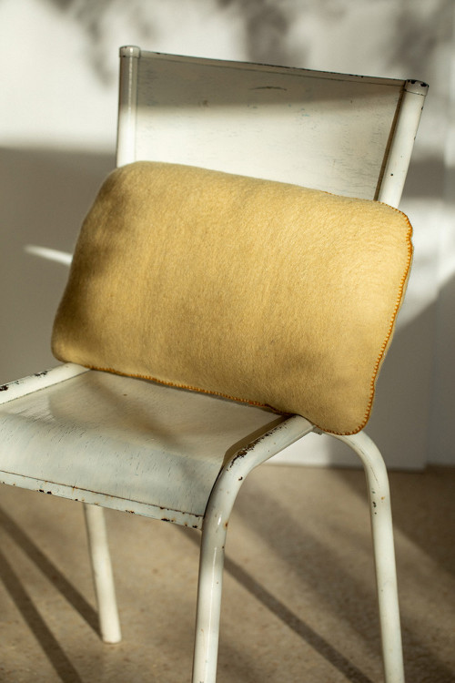 Coussin caillou en laine feutrée posé sur une chaise au soleil