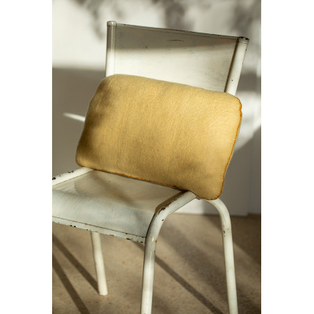 Coussin caillou en laine feutrée posé sur une chaise au soleil