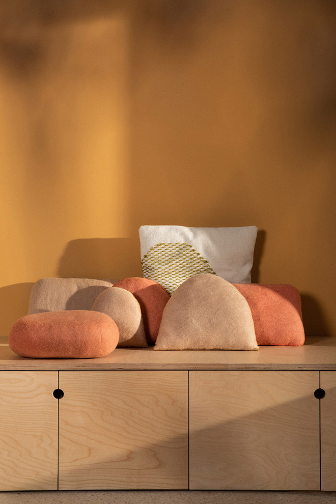 Coussin caillou en laine feutrée posé sur une chaise au soleil
