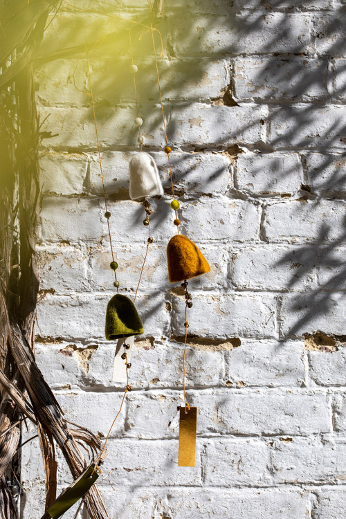 une cloche en feutre or accrochée à un mur en briques blanches