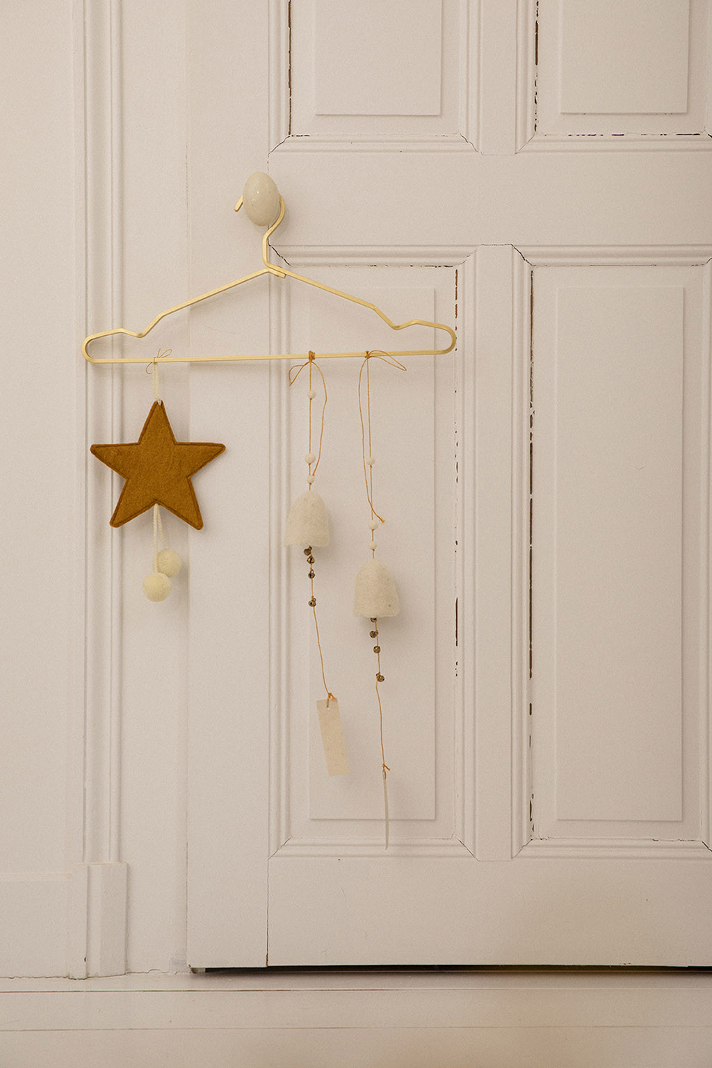 une étoile or en feutre avec des pompons blancs accrochée à la poignée d'une porte pour une touche colorée