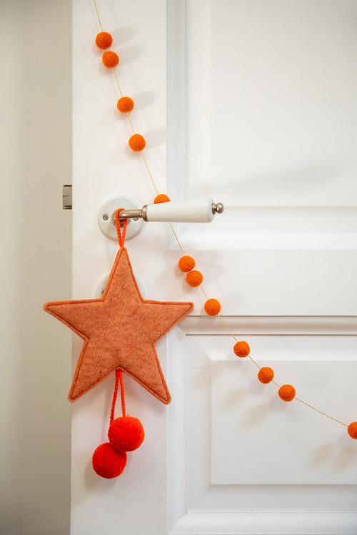 a pink felt star with wool pompons hanging on a door handle for a colorful touch
