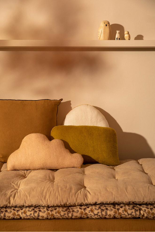 Coussin caillou en laine feutrée posé sur une chaise au soleil
