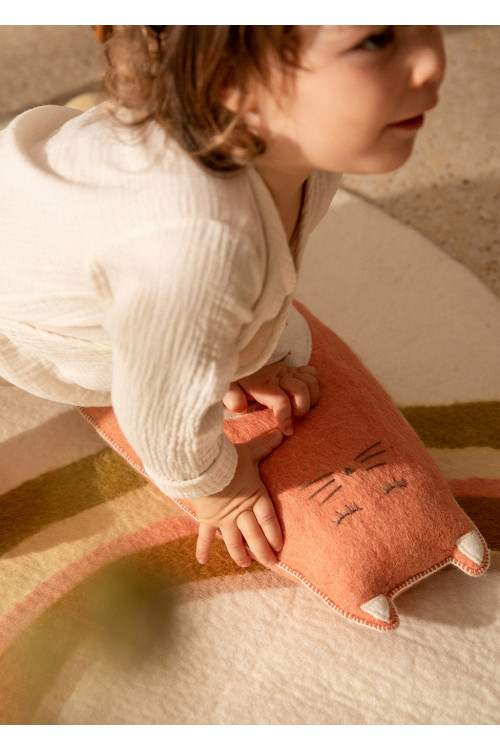 Enfant jouant au sol avec un coussin en forme de chat