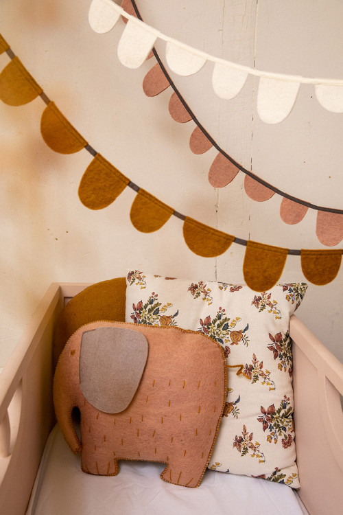 deux guirlandes roses suspendues au dessus d'un coussin éléphant en feutre dans un lit d'enfant