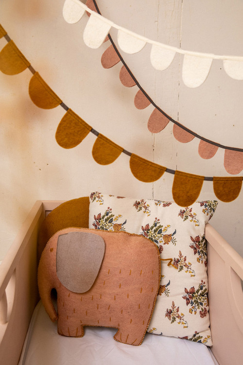 two pink garlands hanging over a felt elephant pillow in a crib