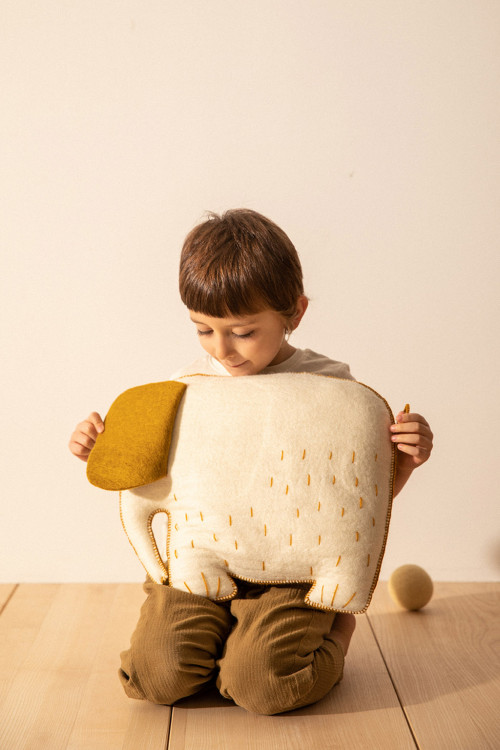 Un enfant joue avec un coussin éléphant en laine feutrée