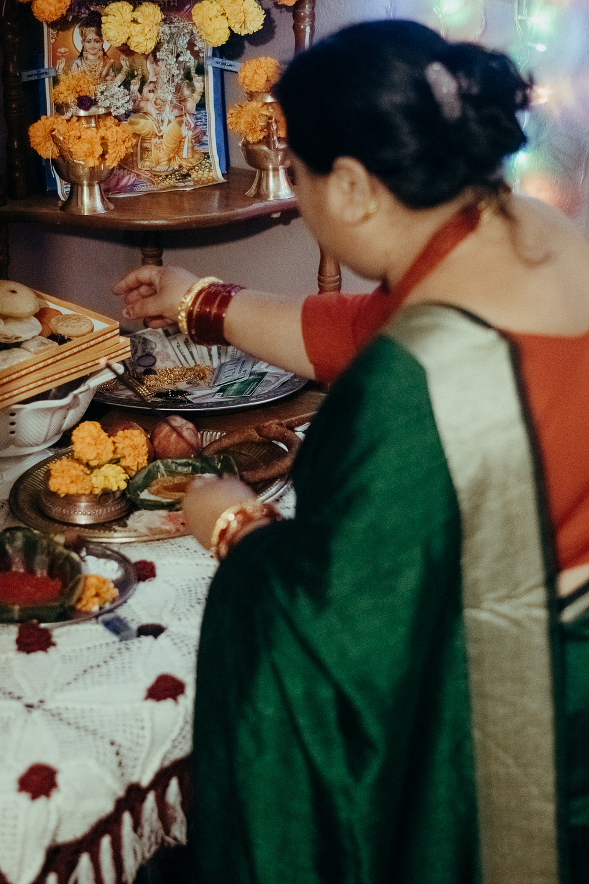 Femme devant un petit autel réalisé avec la représentation de Lakshmi entourée d’une lampe à huile, de fruits, de fleurs, de gâteaux