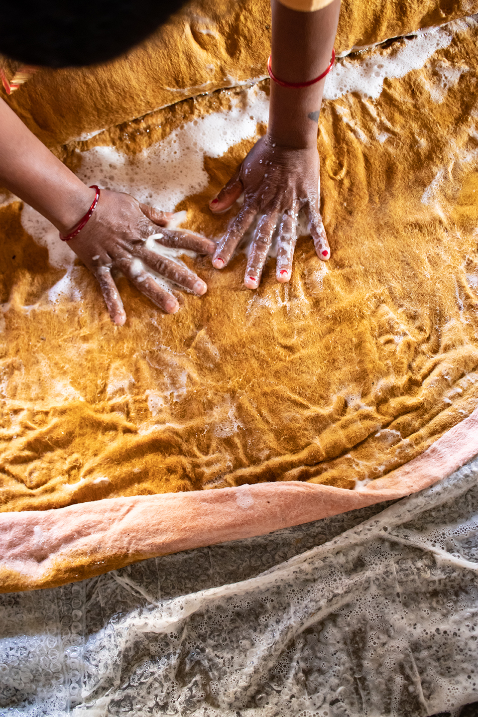 Focus sur les mains d'une artisane népalaise en train de confectionner un tapis rond bicolore en laine feutrée avec de l'eau et du savon