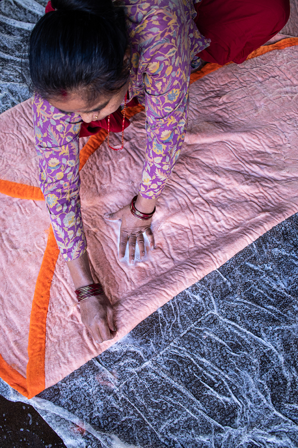 Artisane népalaise en train de confectionner un tapis rond orange et rose en feutre de laine avec de l'eau et du savon