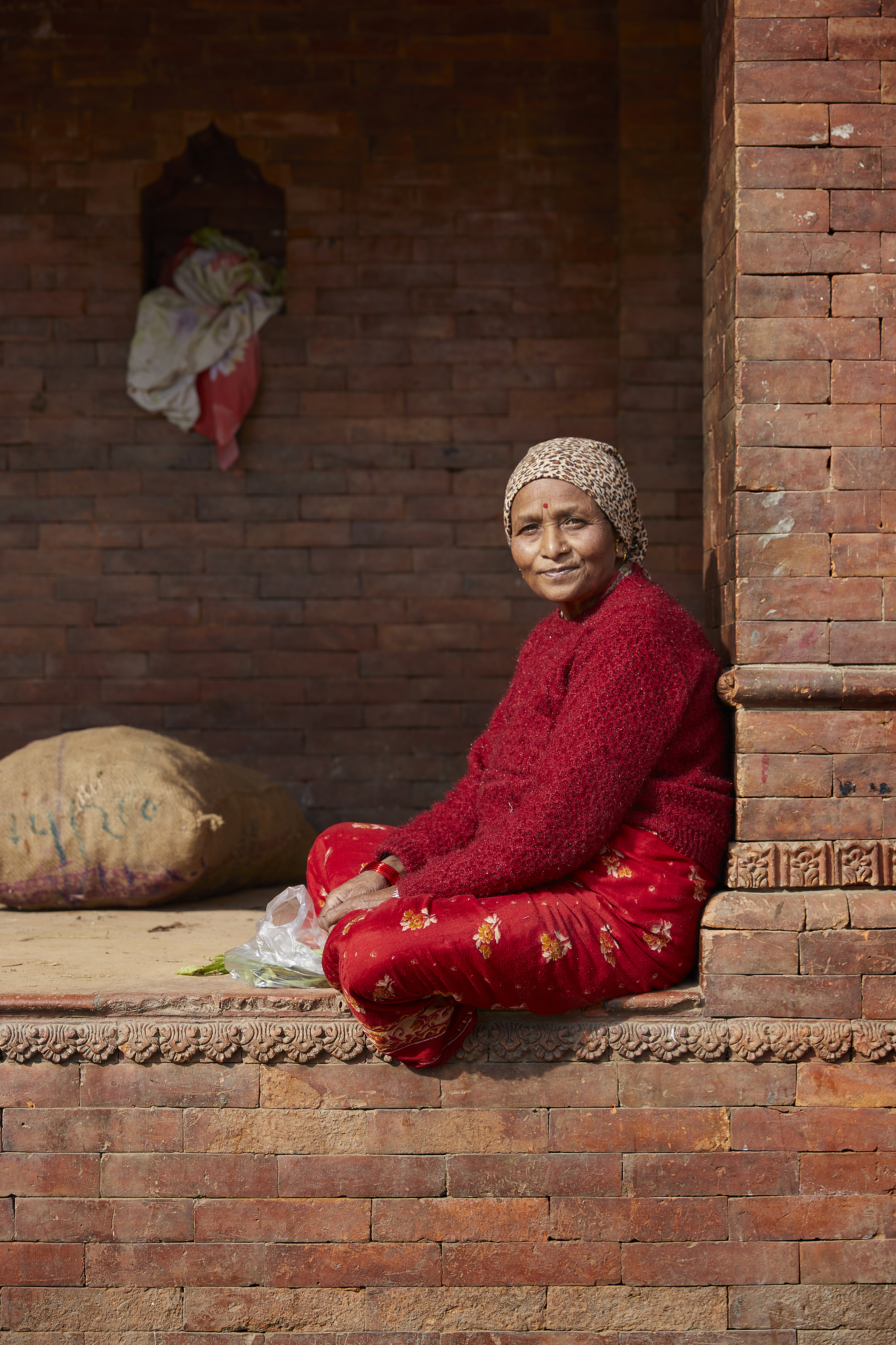 Femme népalaise assise sur un muret regardant l'objectif en souriant