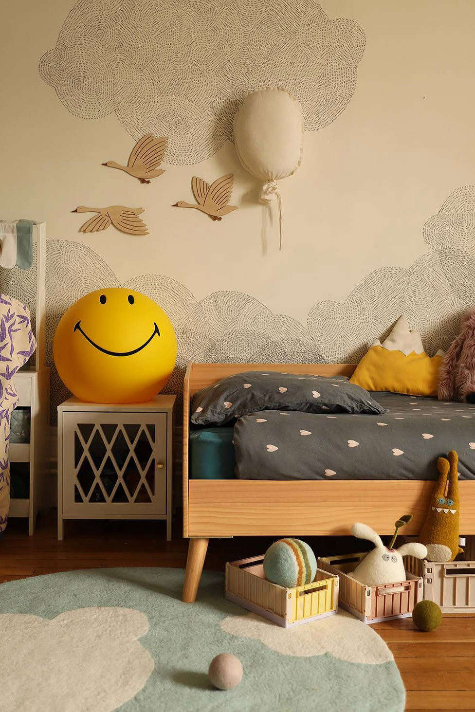 Lit en bois clair et tapis bleu à motif nuage pour chambre d'enfant colorée aux teintes douces