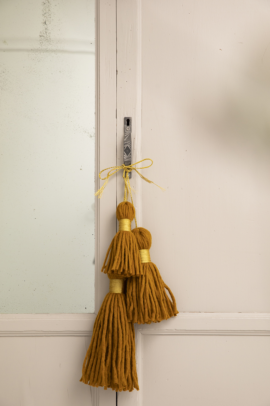 Trio de pompons jaunes décoratifs en laine feutrée accrochés à une poignée d'armoire