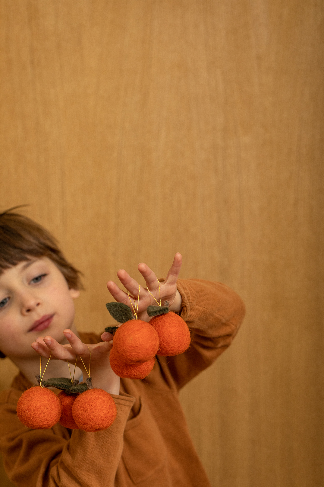 Petit garçon jouant avec des petites décorations clémentines pour le sapin accrochées à ses doigts