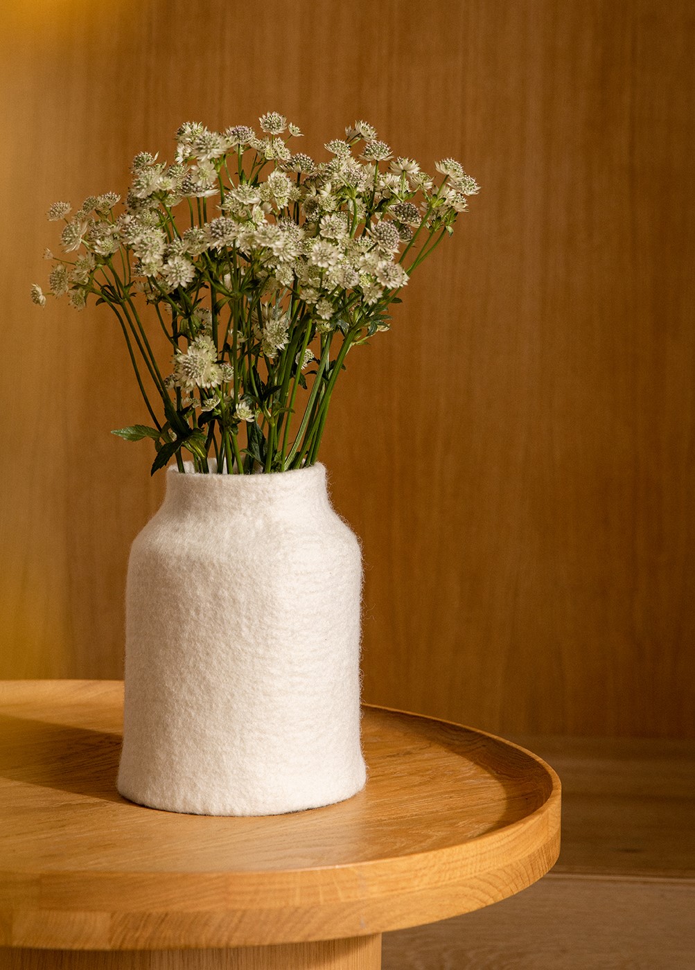 Grand vase blanc en laine bouillie posé sur une table basse ronde dans le salon