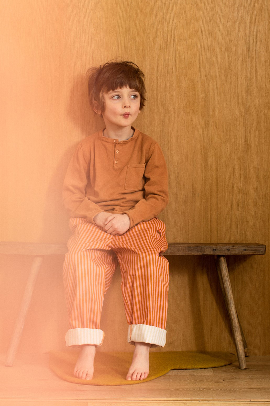 Petit garçon assis sur un banc en bois en pyjama regardant vers la droite