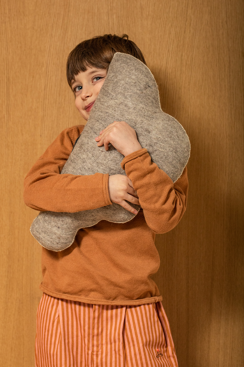 Petit garçon serrant dans ses bras un coussin gris en forme de nuage en laine feutrée