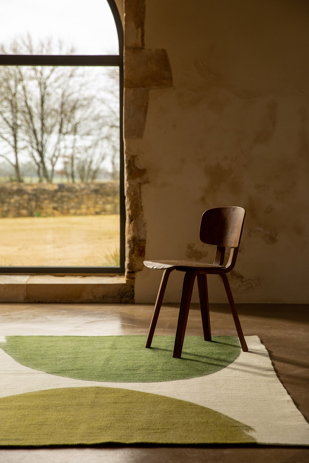 Grand tapis rectangulaire coloré en laine et chaise en bois brut pour une atmosphère minimaliste et apaisante