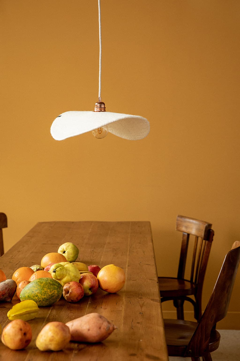 Mur de salle à manger ocre, table en bois et suspension lumineuse plate blanche en feutre de laine