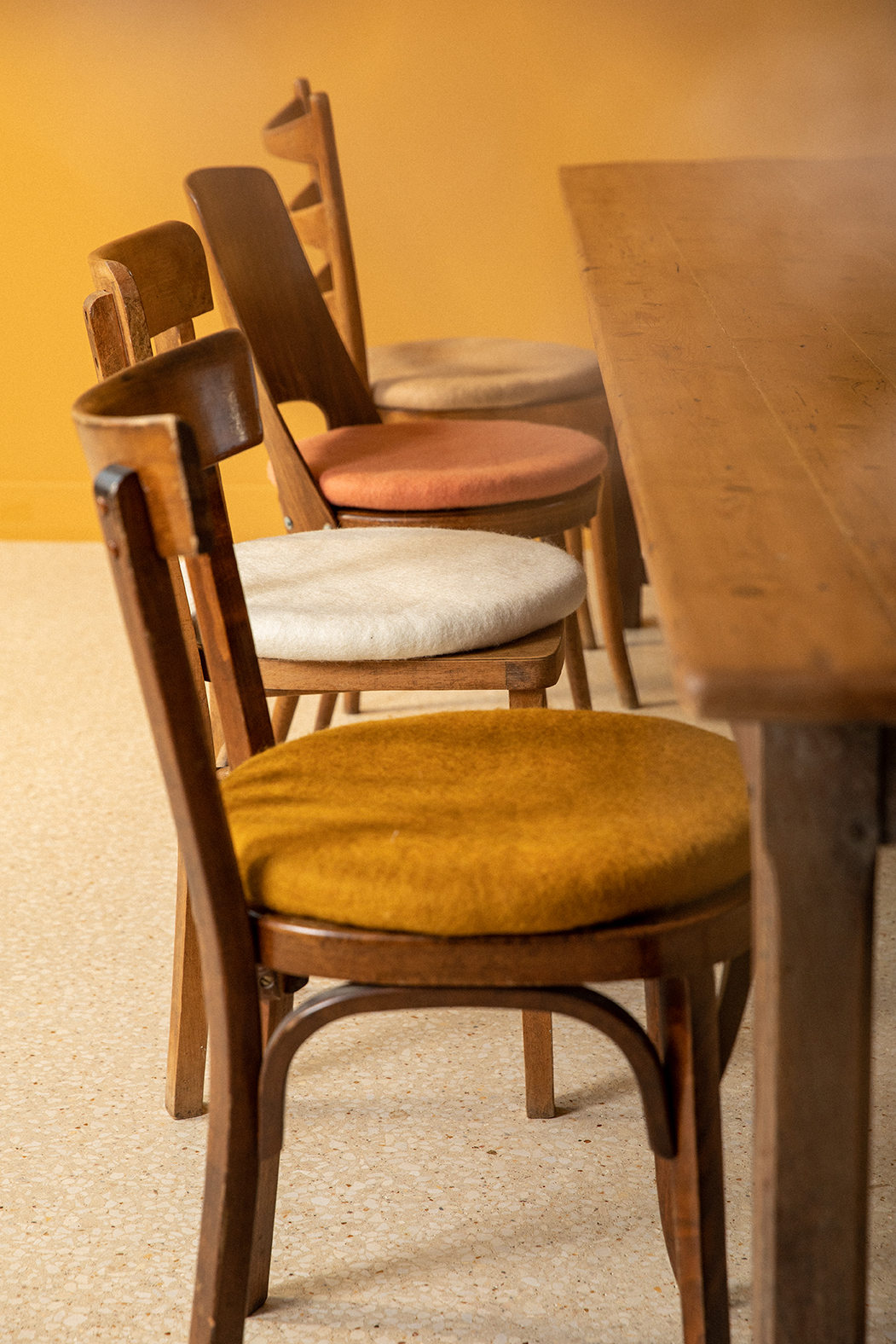 4 coussins ronds jaune, blanc, beige, et rose, en feutre de laine posés sur des chaises de table à manger