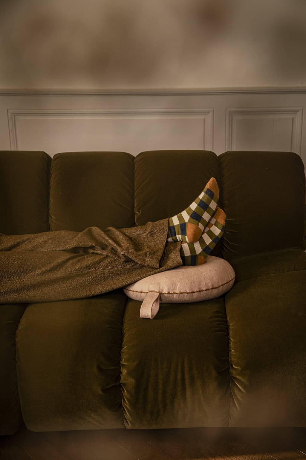Un coussin rond rose poudré en laine sur un canapé kaki